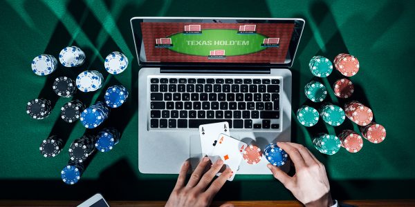 Man playing online poker with laptop on a green table with chips all around, top view